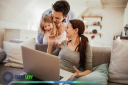 Família sorridente com notebook no colo sentada no sofá, simbolizando o planejamento e controle do orçamento doméstico em ambiente acolhedor.