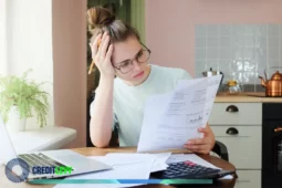 Mulher jovem com expressão preocupada analisando boletos e planilhas em frente ao notebook, representando o desafio de sair das dívidas de forma definitiva.