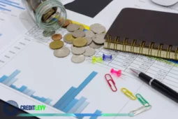 Moedas espalhadas sobre planilhas com gráficos financeiros, caderno, caneta e clipes, representando o planejamento de investimentos para iniciantes.