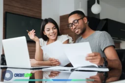 Casal sorridente sentado à mesa analisando documentos financeiros juntos, com notebook e pastas, representando o planejamento de finanças para casais.
