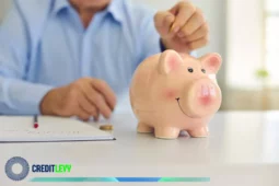 Pessoa colocando moeda em cofre de porquinho sorridente sobre uma mesa, representando o hábito de poupar e investir em previdência privada para o futuro.