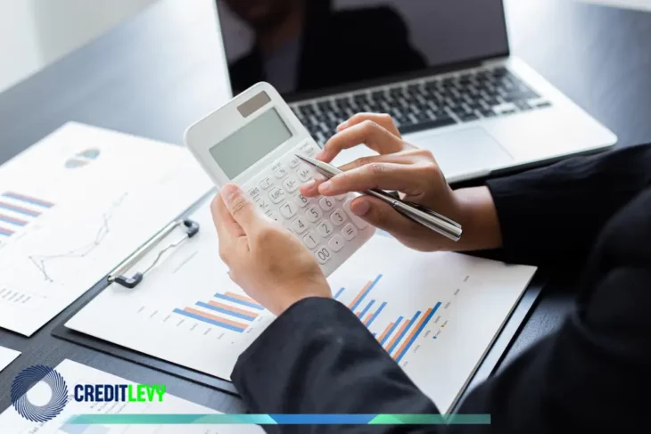Pessoa calculando sobre gráficos financeiros com laptop ao fundo, simbolizando análise e tomada de decisão em investimentos de renda variável.