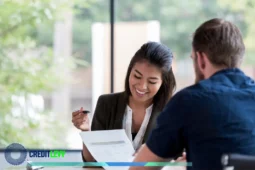 Consultora financeira sorridente explicando tipos de empréstimo para cliente com documentos em mãos, em ambiente profissional e iluminado.