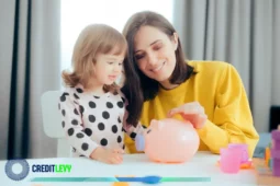 Mãe e filha sorrindo enquanto colocam moedas em um cofrinho rosa, representando o início da educação financeira para jovens.