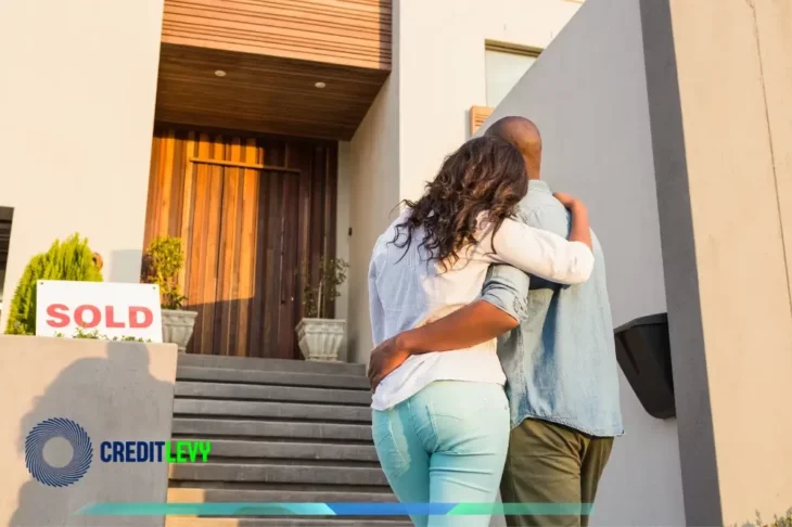 Pareja abrazada frente a su nueva casa con cartel de 