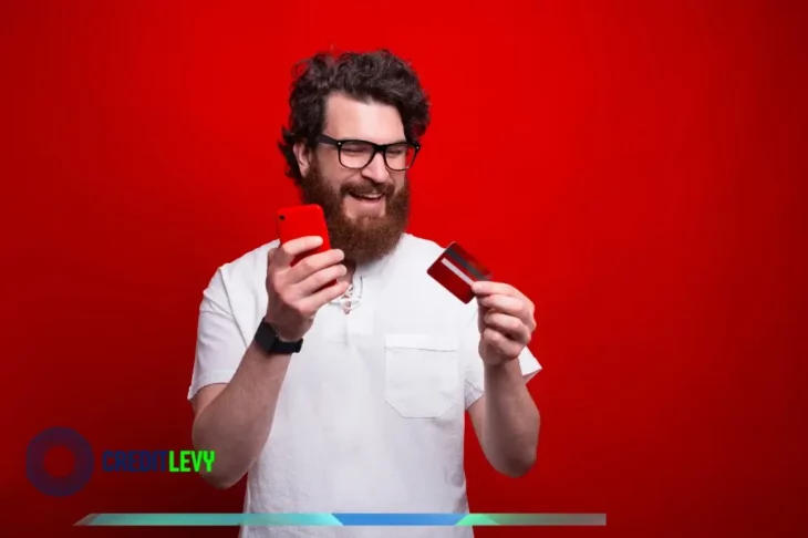 Hombre sonriente con móvil y tarjeta de crédito en la mano, representando el uso responsable de la tarjeta de crédito con sabiduría.