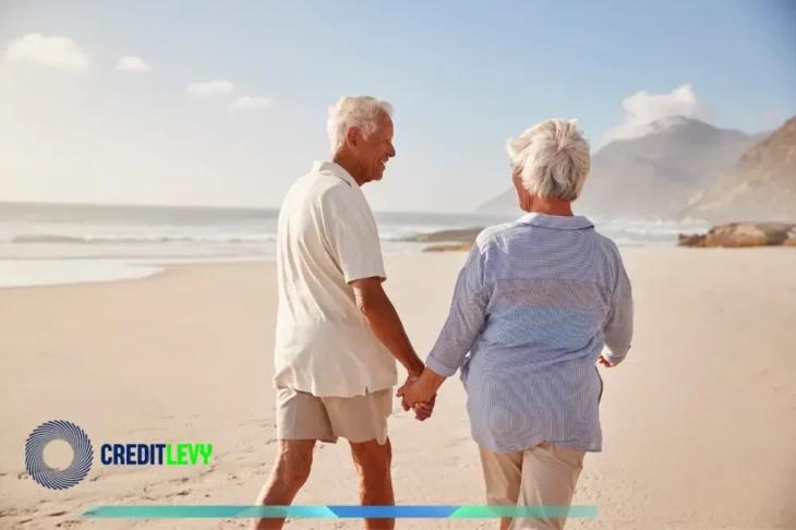 Pareja de adultos mayores caminando de la mano por la playa, representando el concepto de planeando la jubilación ideal y el disfrute de un retiro seguro.