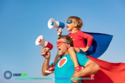 Pai e filho vestidos de super-heróis erguendo megafones sob céu azul, comemorando o Dia dos Pais com alegria e criatividade.