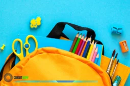 Mochila amarilla abierta con útiles coloridos sobre fondo azul, lista para el regreso a clases