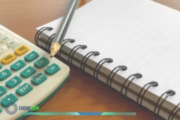 Fotografia de uma calculadora com botões verdes, um caderno espiral aberto e um lápis sobre uma mesa de madeira, com a logomarca “CREDITLEVY” no canto inferior esquerdo.