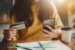 Mujer con tarjeta y celular revisa costos ocultos de su tarjeta de crédito.