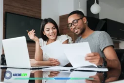 Casal analisando documentos e sorrindo em frente a um notebook, simbolizando o planejamento financeiro e o bom uso do 13º salário.