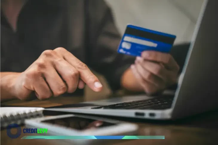 Persona usando una laptop y sosteniendo una tarjeta de crédito, representando el cálculo y control de los intereses de la tarjeta de crédito.