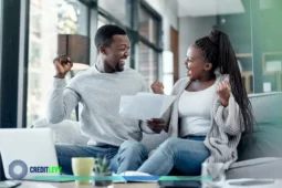 Casal feliz segurando documento e comemorando a quitação de dívidas, representando o Feirão Limpa Nome e a oportunidade de renegociar contas em atraso.