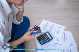 Pessoa segurando vários cartões de crédito ao lado de contas e calculadora, representando preocupação com Dívida de Fim de Ano.