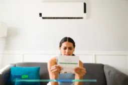 Mulher sentada no sofá analisando a conta de luz com expressão de preocupação enquanto o ar condicionado está ligado ao fundo