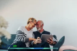 Aposentadoria, casal de idosos sentado no sofá usando um tablet e conversando com sorriso.